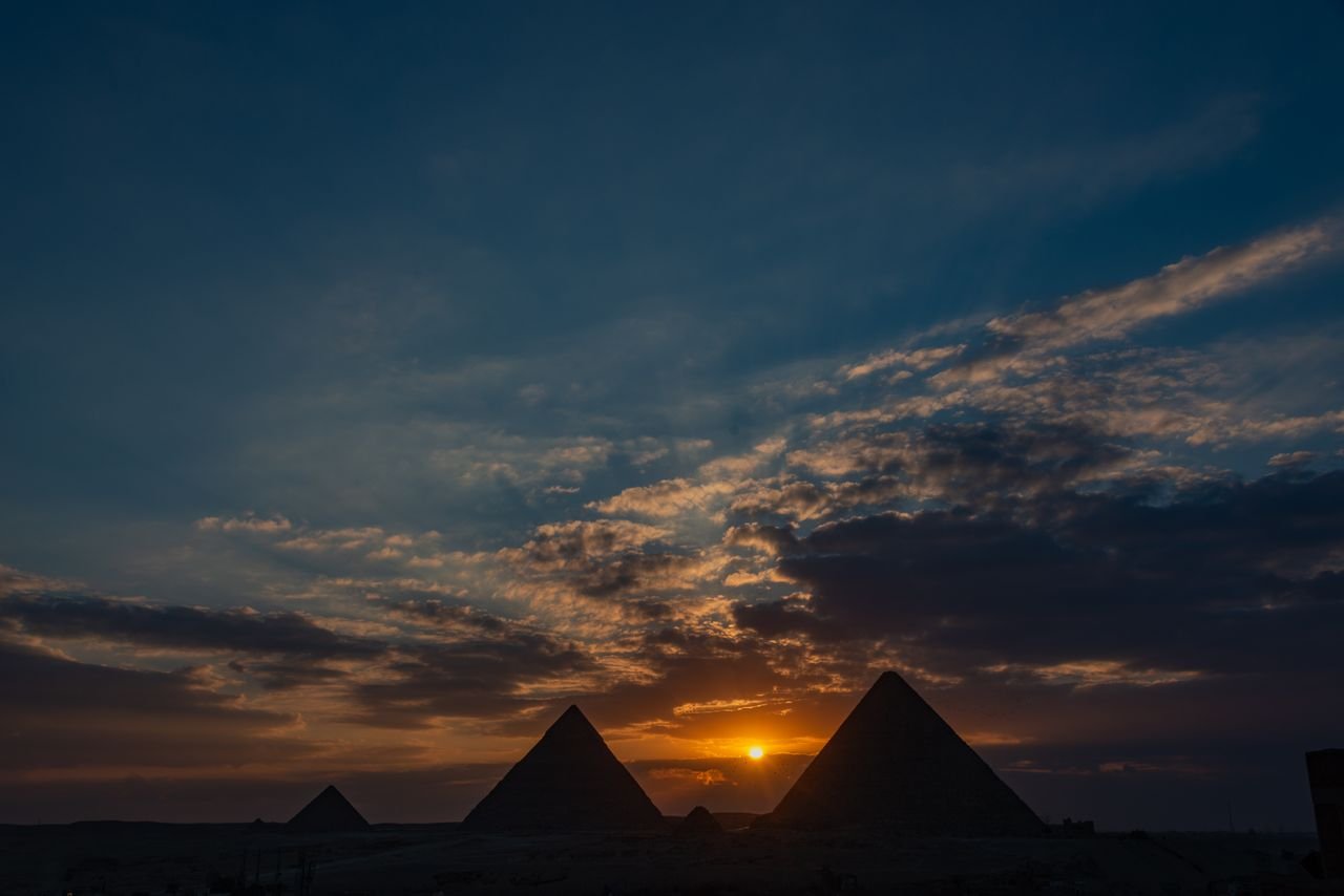 Silhouette of Giza pyramids against a dramatic sunset sky.