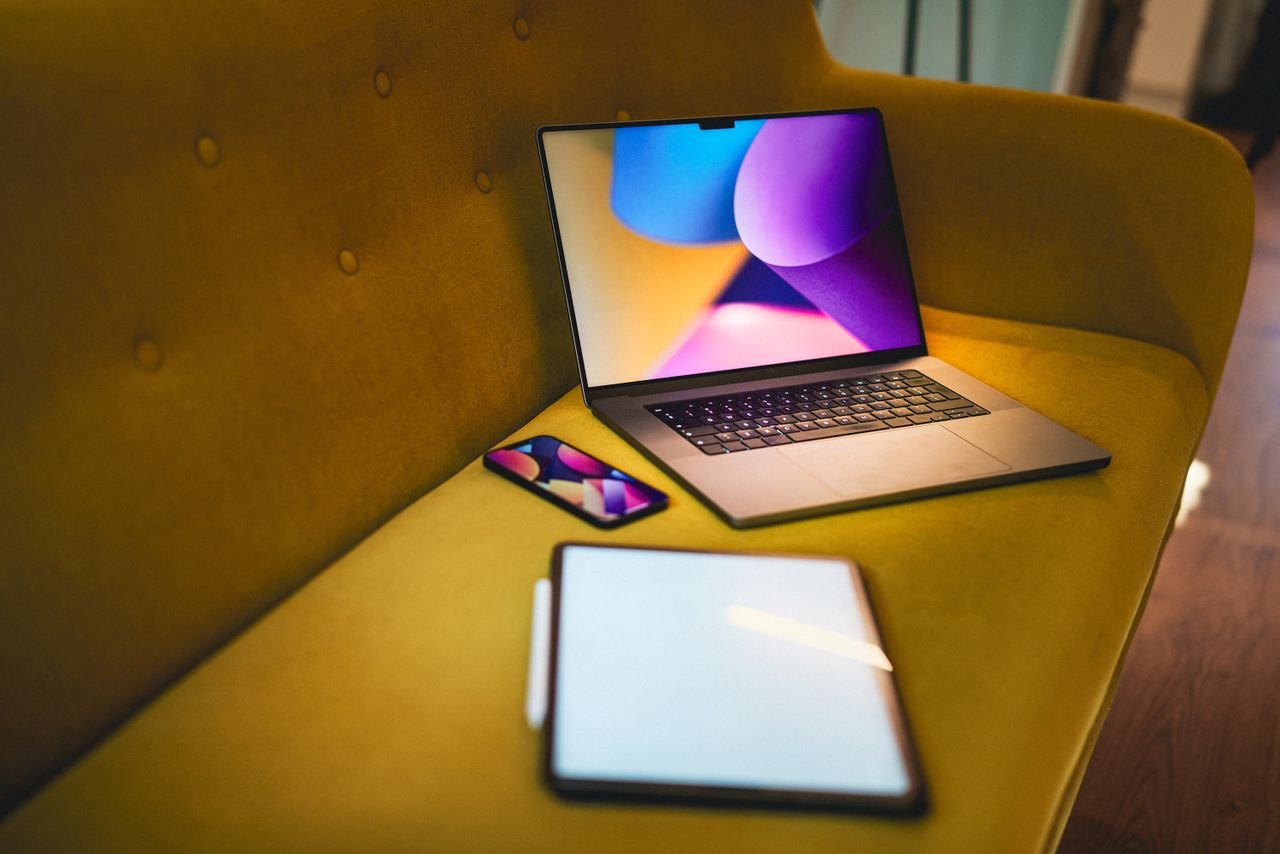 A cozy home office setting with a laptop, smartphone, and tablet on a yellow sofa.