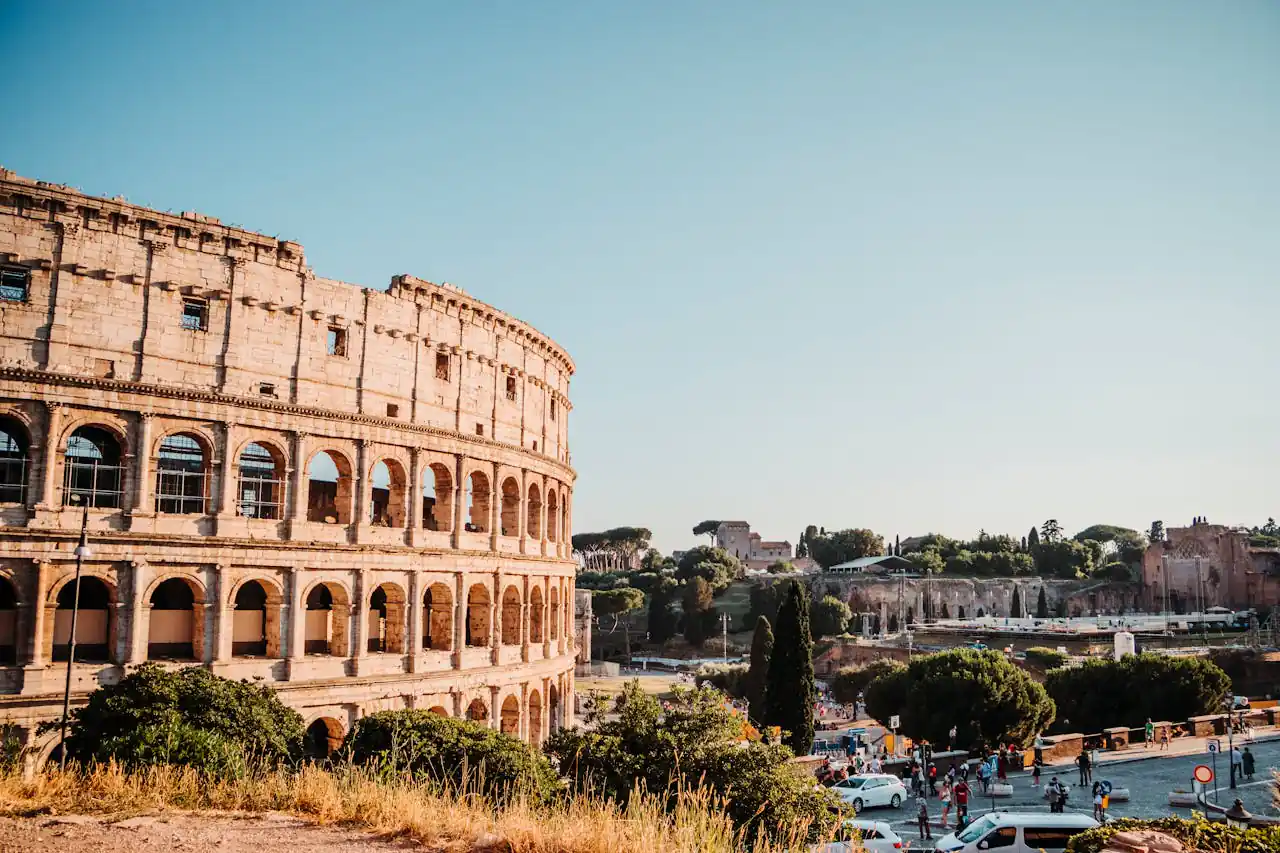 The iconic Colosseum in Rome, a historic amphitheater surrounded by urban scenery on a bright day.