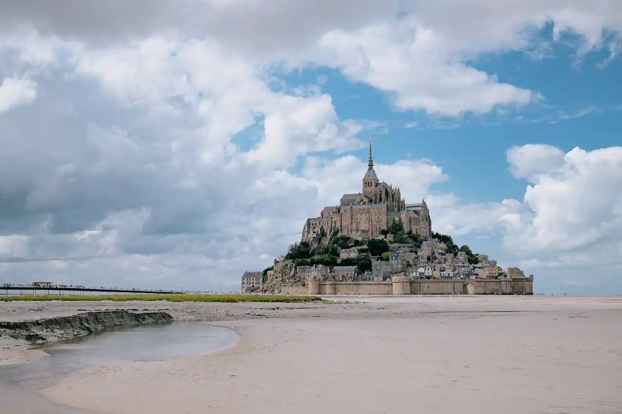 Breathtaking landscape of Mont Saint-Michel surrounded by sandy shores and blue skies.